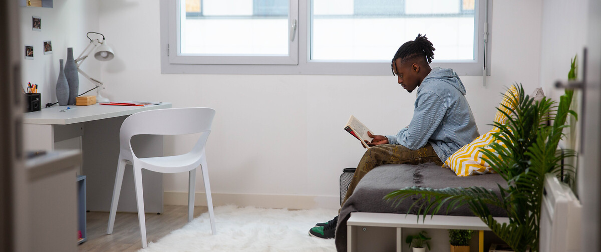 Etudiant lisant un livre dans son appartement étudiant Paris La Défense Grande Arche